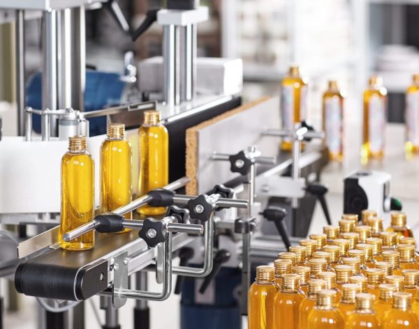 Horizontal shot of cosmetics or pharmacy plant with automated equipment. Transparent plastic bottles filled with yellow substance standing on desk and conveyor line, ready for transportation