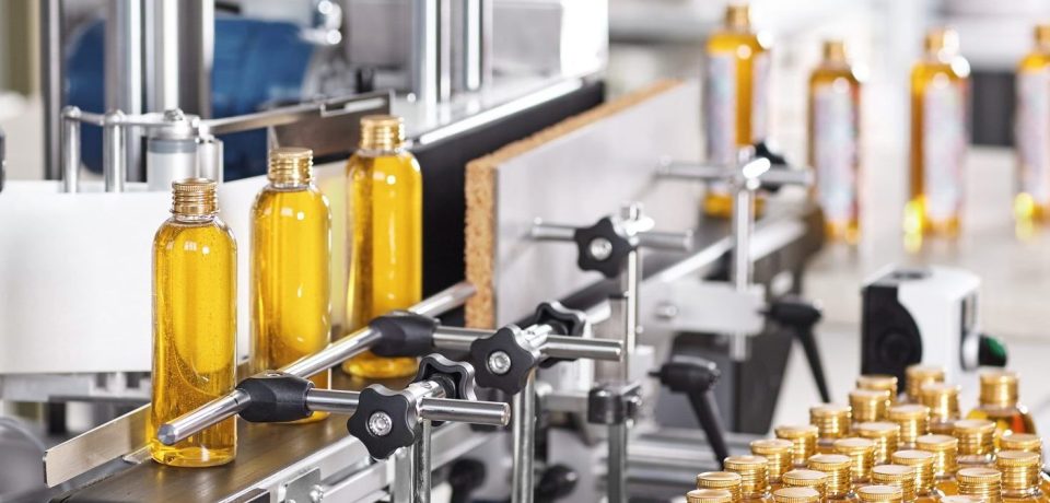 Horizontal shot of cosmetics or pharmacy plant with automated equipment. Transparent plastic bottles filled with yellow substance standing on desk and conveyor line, ready for transportation